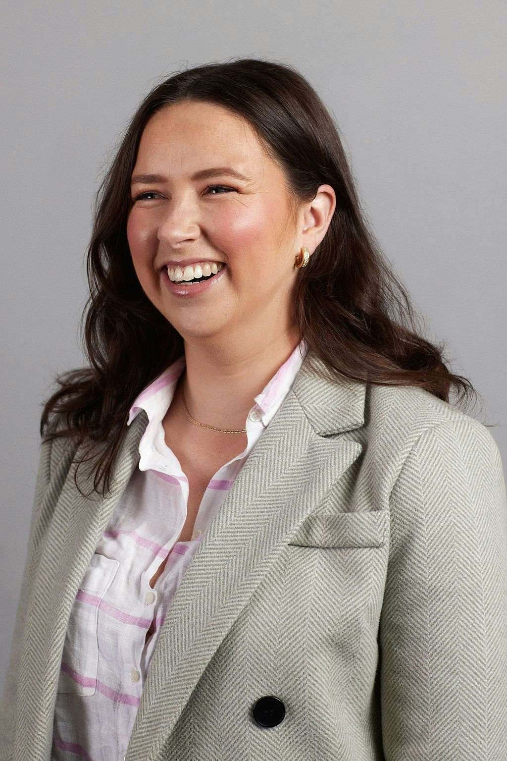 Headshot of Hannah smiling and wearing a white shirt and grey blazer.
