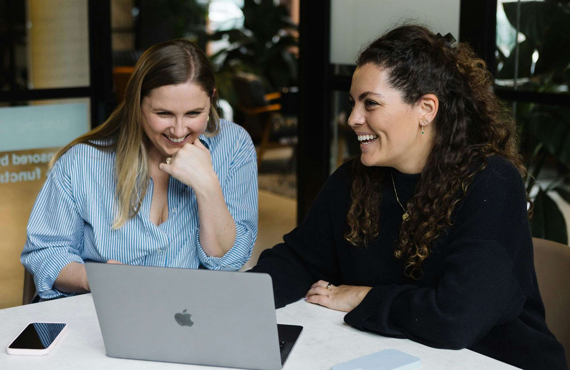 Two women working together and smiling with a laptop on the table.